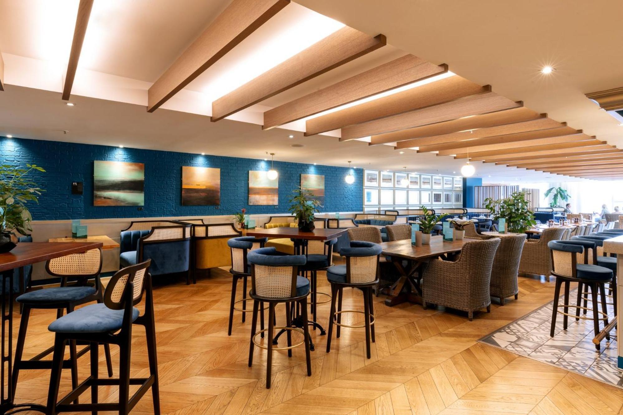 Voco St. David'S Cardiff By Ihg Hotel Buitenkant foto The photo shows a modern dining or lounge area with a stylish interior design. The space features wooden ceiling beams and a combination of different seating arrangements, including high-backed bar stools and cozy dining chairs around tables. The wal