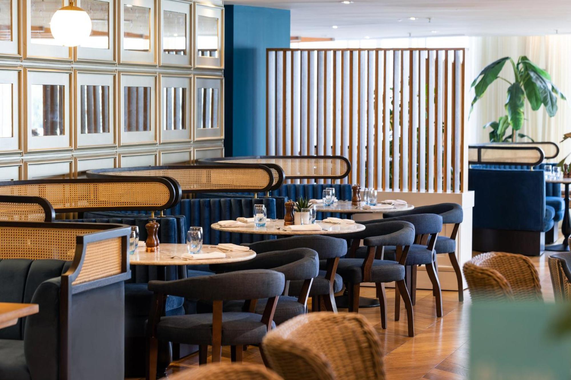 Voco St. David'S Cardiff By Ihg Hotel Buitenkant foto The photo depicts a stylish dining area with several tables set for meals. The seating includes dark blue upholstered benches and wooden chairs with a modern design. There are decorative elements such as mirrors on the wall and a wooden slatted parti