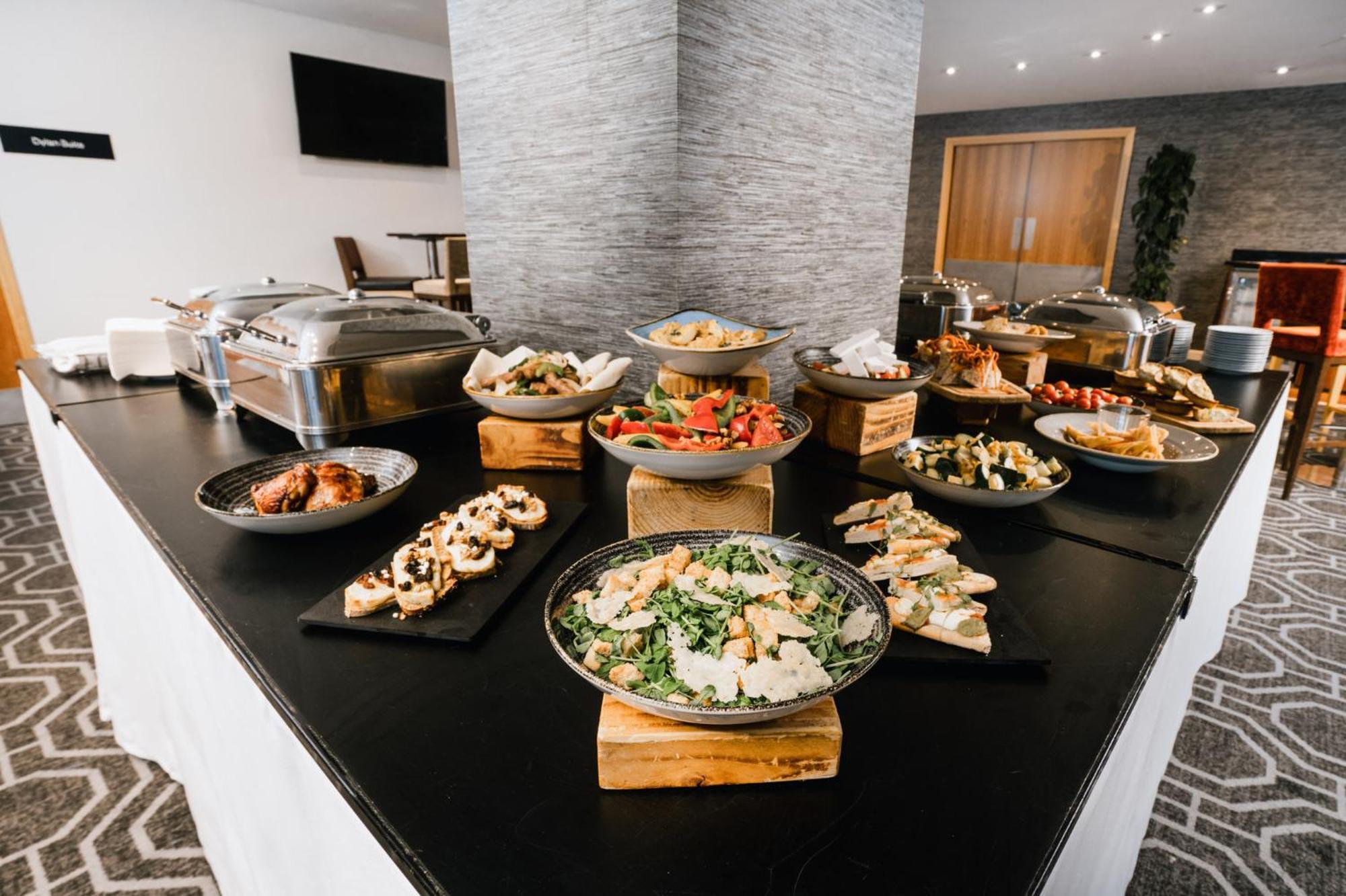 Voco St. David'S Cardiff By Ihg Hotel Buitenkant foto The photo shows a buffet setup featuring a variety of food items displayed on a large table. There are multiple serving dishes with different types of food, including salads, appetizers, and possibly main dishes. The items are presented on both woode